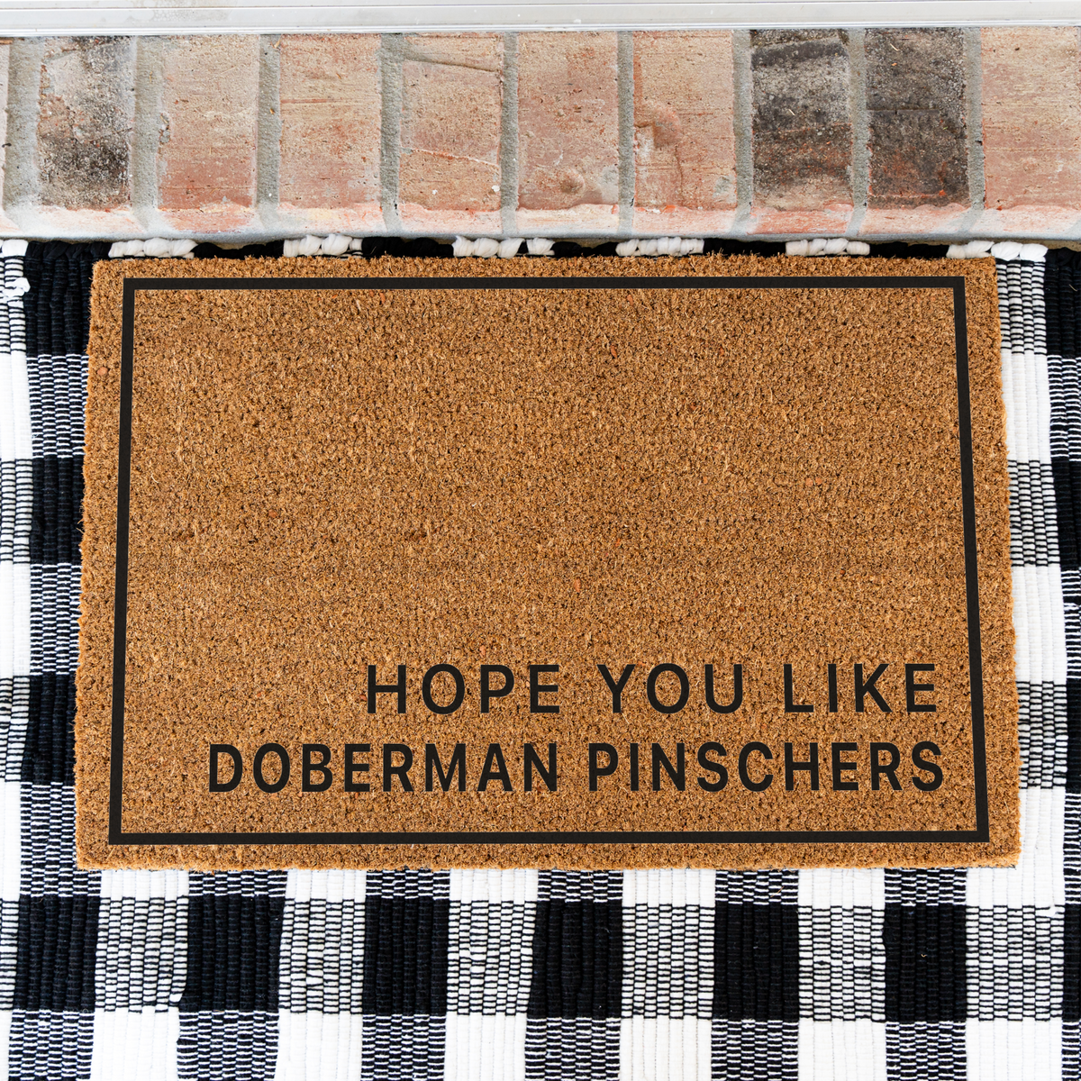 Hope You Like Doberman Pinschers minimalist coir doormat with a thin black border on a black and white buffalo check rug, close view