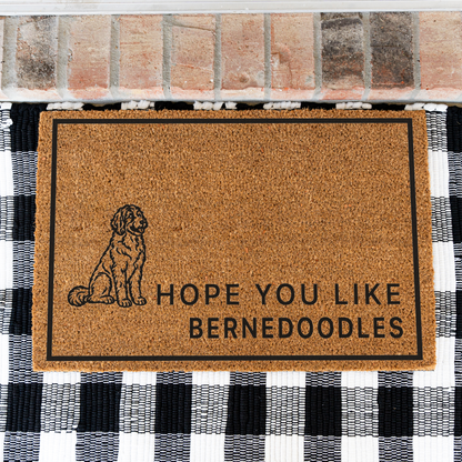 Hope You Like Bernedoodles coir doormat with a drawing of a sitting Bernedoodle on a black and white buffalo check rug, close view