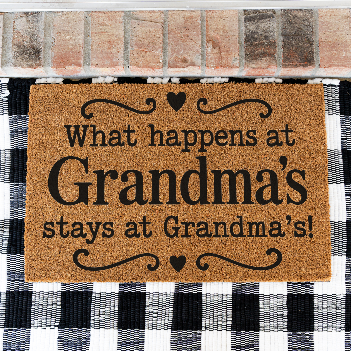 What Happens at Grandma's Stays at Grandma's coir doormat with hearts on a black and white buffalo check rug, close view