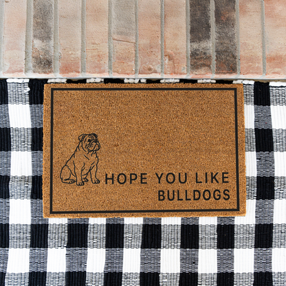 Hope You Like Bulldogs coir doormat with a drawing of a sitting bulldog on a black and white buffalo check rug at a brick step