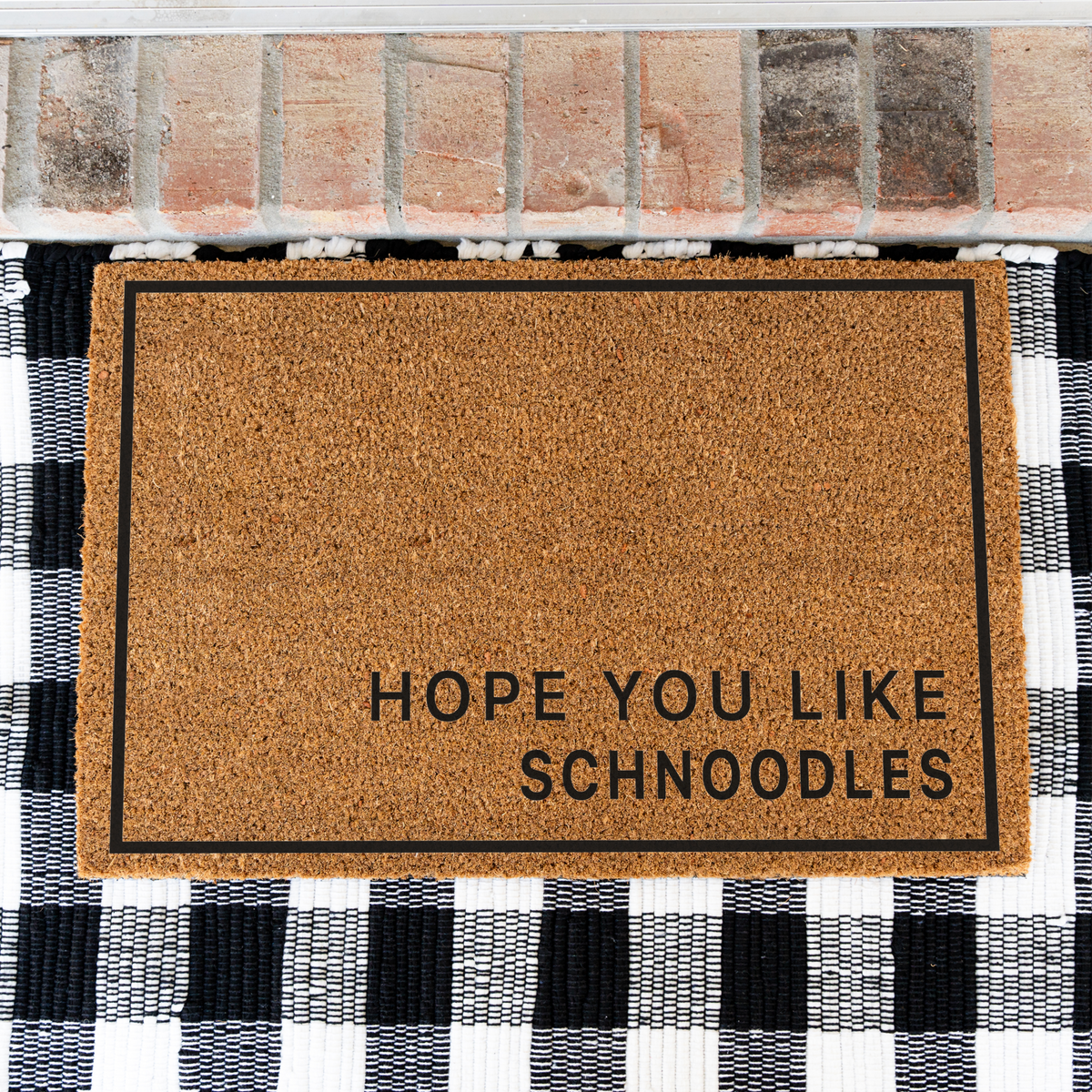 Hope You Like Schnoodles minimalist coir doormat with a thin black border on a black and white buffalo check rug, close view