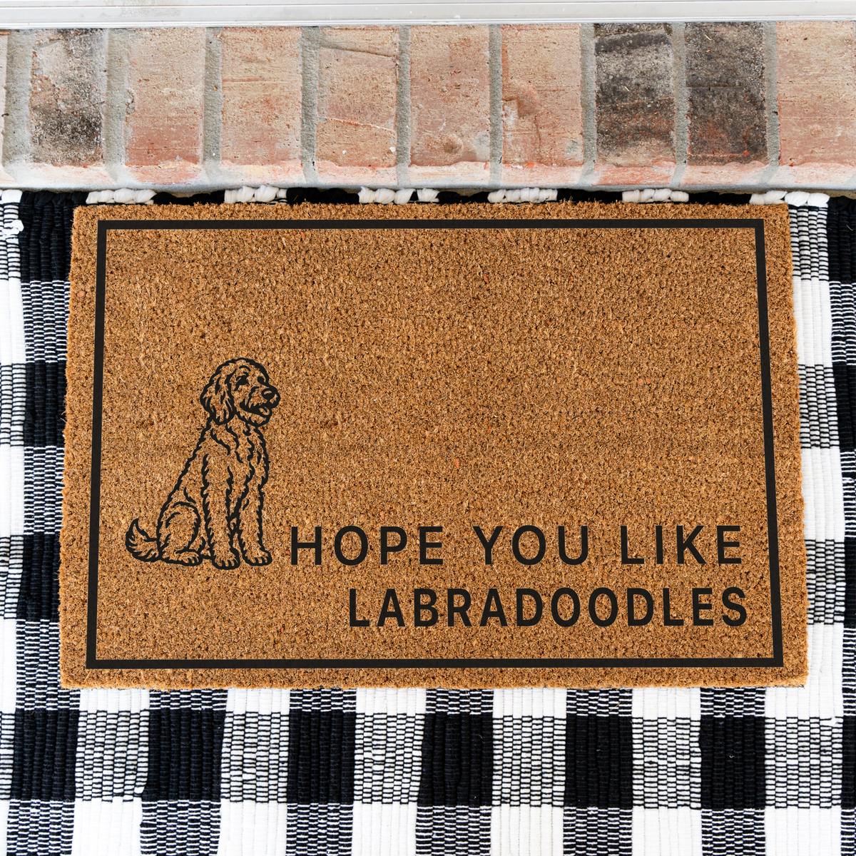 Hope You Like Labradoodles coir doormat with a drawing of a sitting Labradoodle on a black and white buffalo check rug, close view