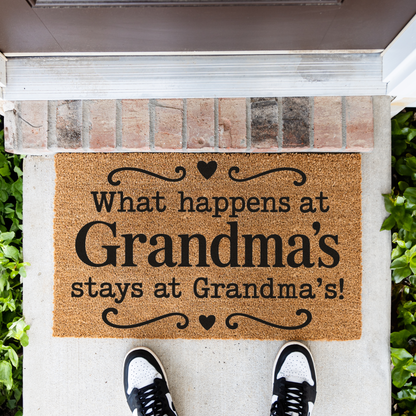 What Happens at Grandma's Stays at Grandma's coir doormat with hearts in front of a brick step, top-down view