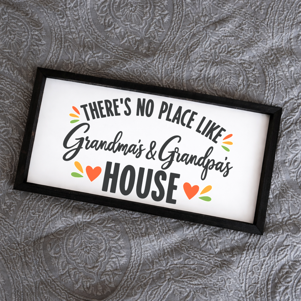 There's No Place Like Grandma's & Grandpa's House wide framed sign with a black frame on a grey quilted bedspread