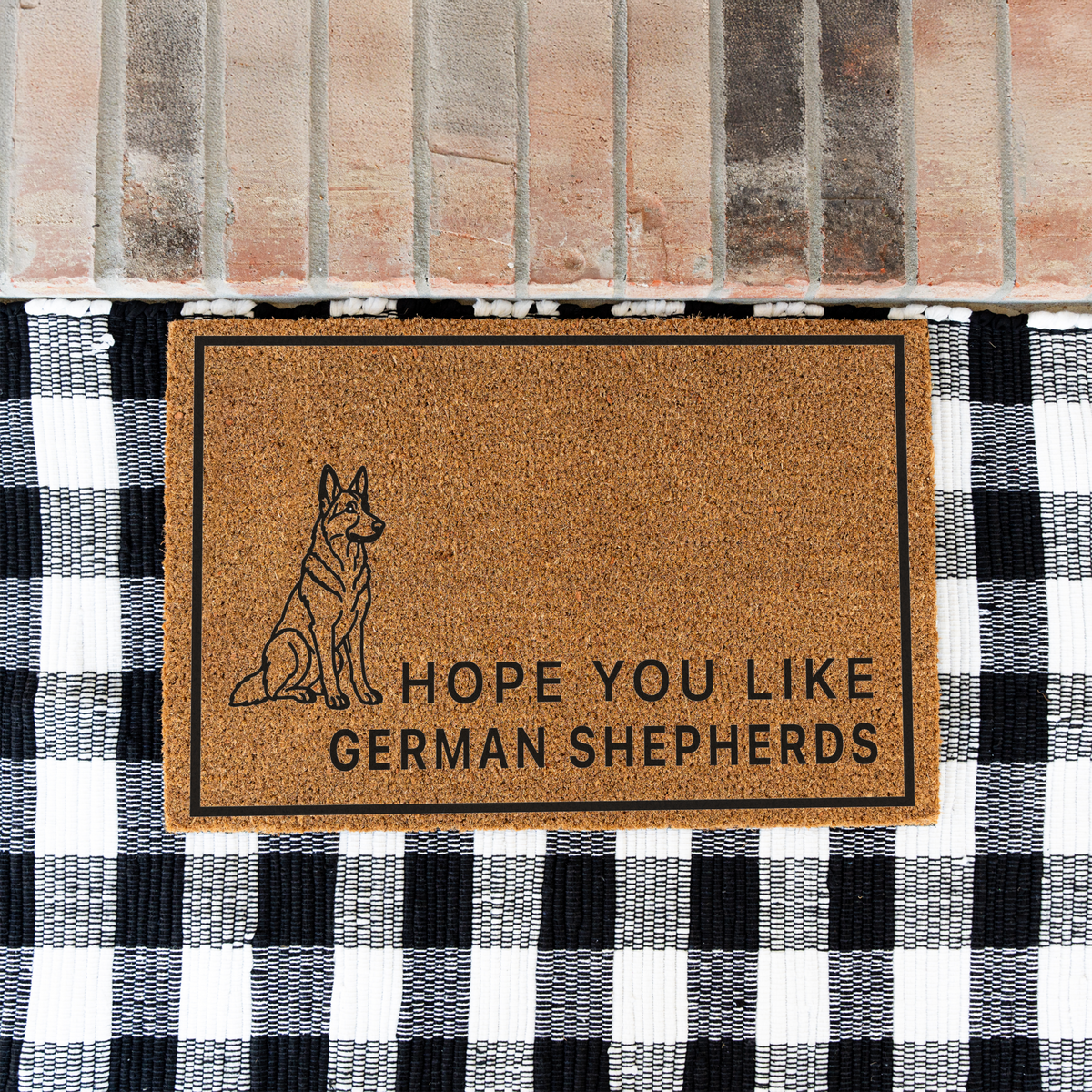 Hope You Like German Shepherds coir doormat with a drawing of a sitting German shepherd on a black and white buffalo check rug at a brick step