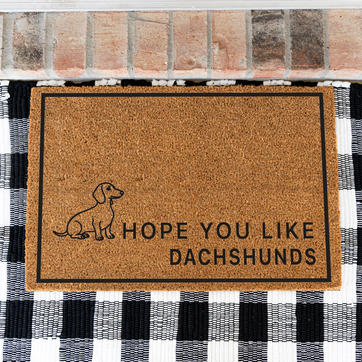 Hope You Like Dachshunds coir doormat with a drawing of a sitting dachshund on a black and white buffalo check rug, close view