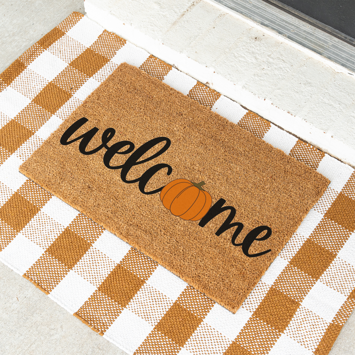Welcome pumpkin coir doormat on a tan and white check rug