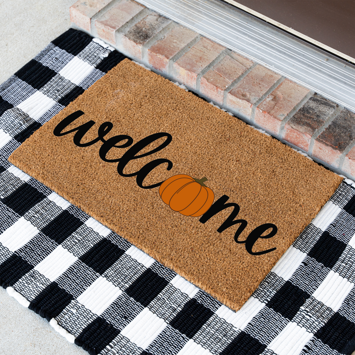 Welcome pumpkin coir doormat at an angle on a black and white buffalo check rug