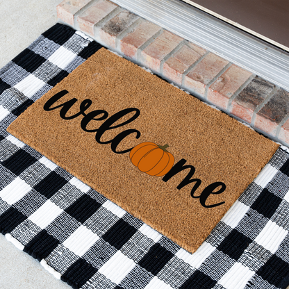 Welcome pumpkin coir doormat at an angle on a black and white buffalo check rug