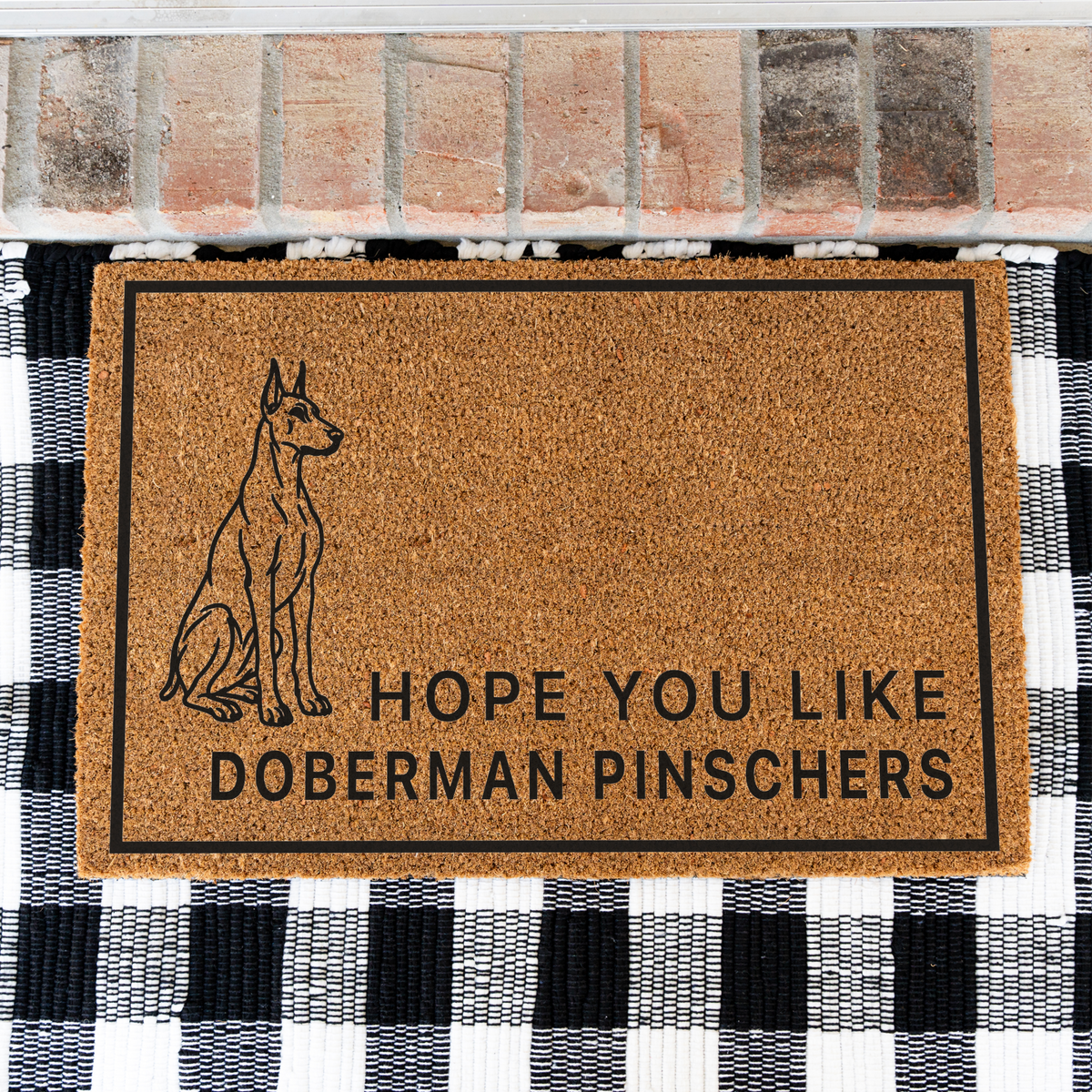 Hope You Like Doberman Pinschers coir doormat with a drawing of a sitting Doberman pinscher on a black and white buffalo check rug, close view
