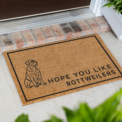 Hope You Like Rottweilers coir doormat with a drawing of a sitting Rottweiler at an angle on a front porch by a brick step
