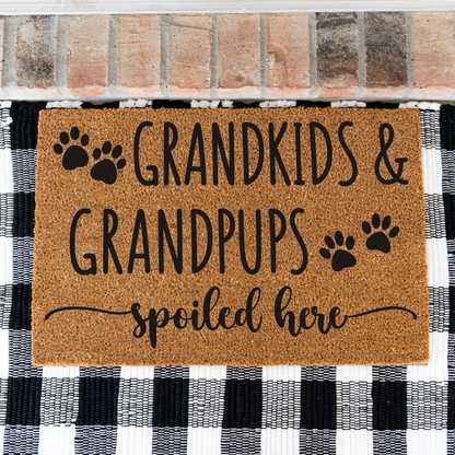 Grandkids & Grandpups Spoiled Here coir doormat with paw prints on a black and white buffalo check rug, close view