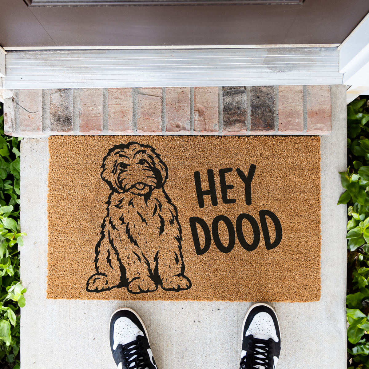 Hey Dood doodle dog coir doormat in front of a brick step, top-down view