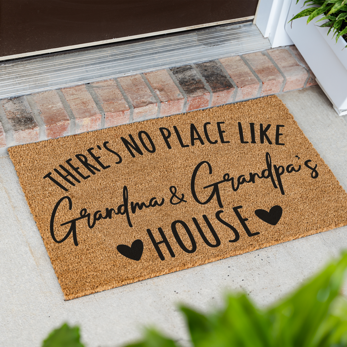 There's No Place Like Grandma & Grandpa's House coir doormat at an angle on a front porch by a brick step