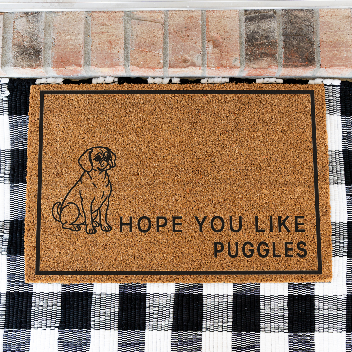 Hope You Like Puggles coir doormat with a drawing of a sitting Puggle on a black and white buffalo check rug, close view