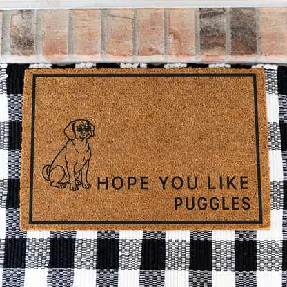 Hope You Like Puggles coir doormat with a drawing of a sitting Puggle on a black and white buffalo check rug, close view