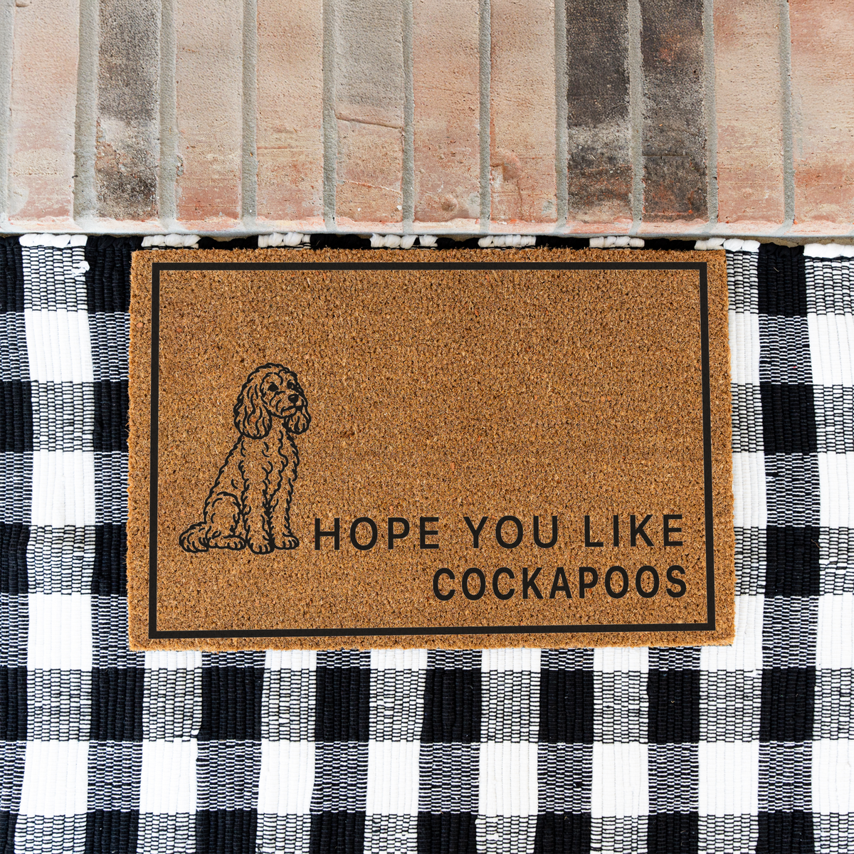 Hope You Like Cockapoos coir doormat with a drawing of a sitting Cockapoo on a black and white buffalo check rug at a brick step