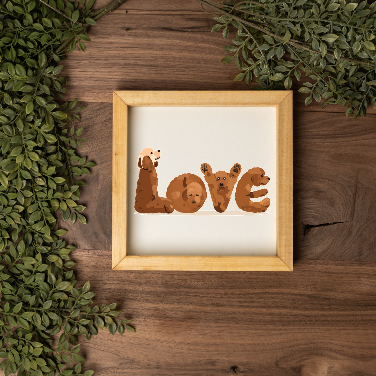 Four red doodles spelling LOVE square framed sign with a natural wood frame on a dark wood table with greenery