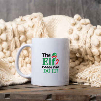 The Elf Made Me Do It white ceramic Christmas coffee mug next to a cream knit blanket