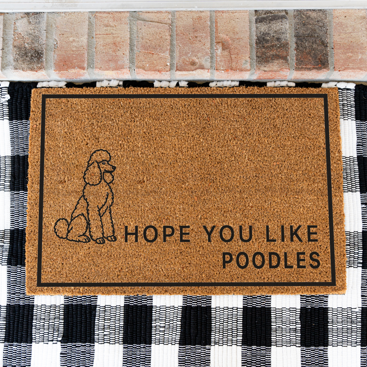 Hope You Like Poodles coir doormat with a drawing of a sitting poodle on a black and white buffalo check rug, close view