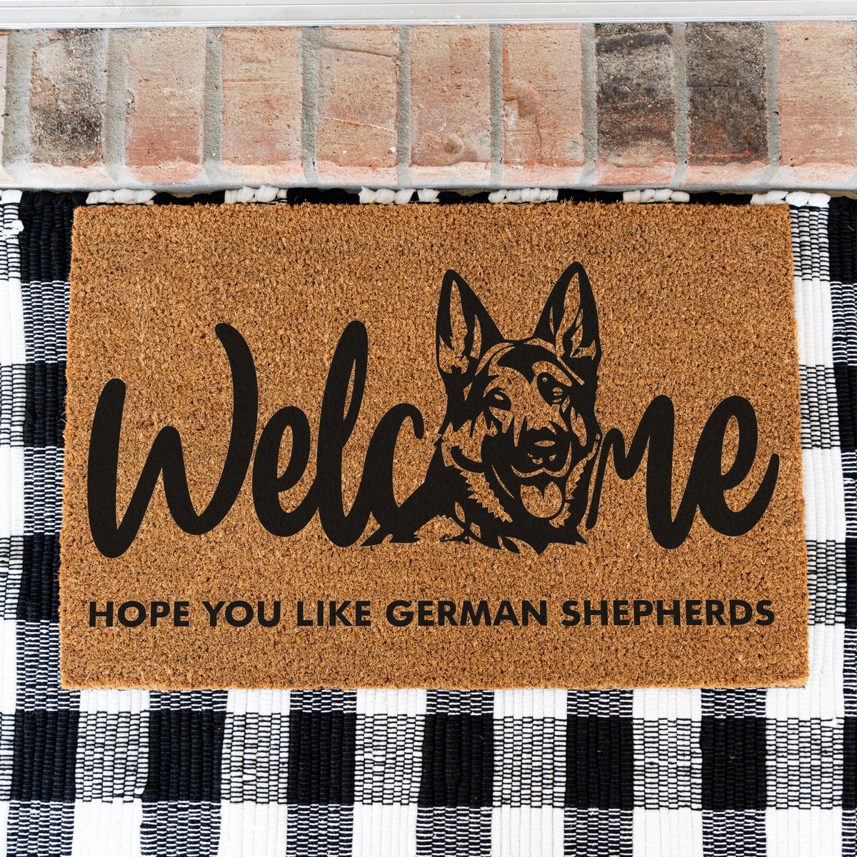Welcome Hope You Like German Shepherds coir doormat with a German shepherd head in the word welcome on a black and white buffalo check rug, close view