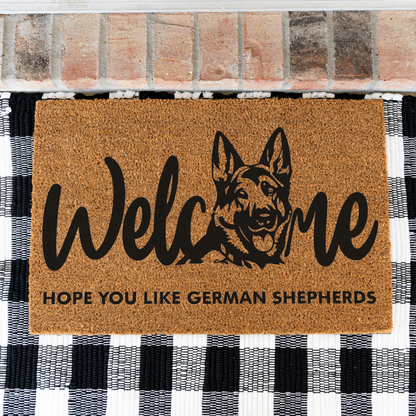 Welcome Hope You Like German Shepherds coir doormat with a German shepherd head in the word welcome on a black and white buffalo check rug, close view