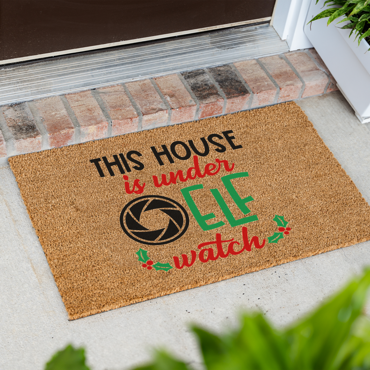 This House Is Under Elf Watch coir doormat at an angle in front of a brick step