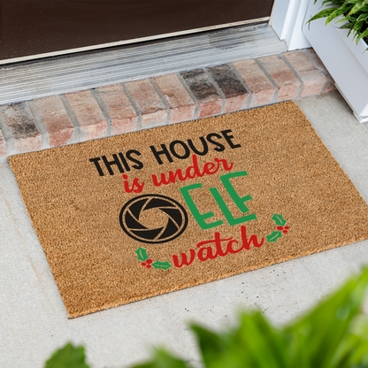 This House Is Under Elf Watch coir doormat at an angle in front of a brick step
