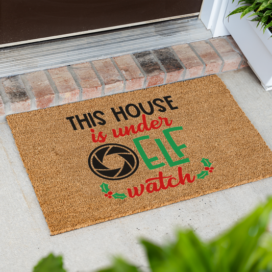 This House Is Under Elf Watch coir doormat at an angle in front of a brick step