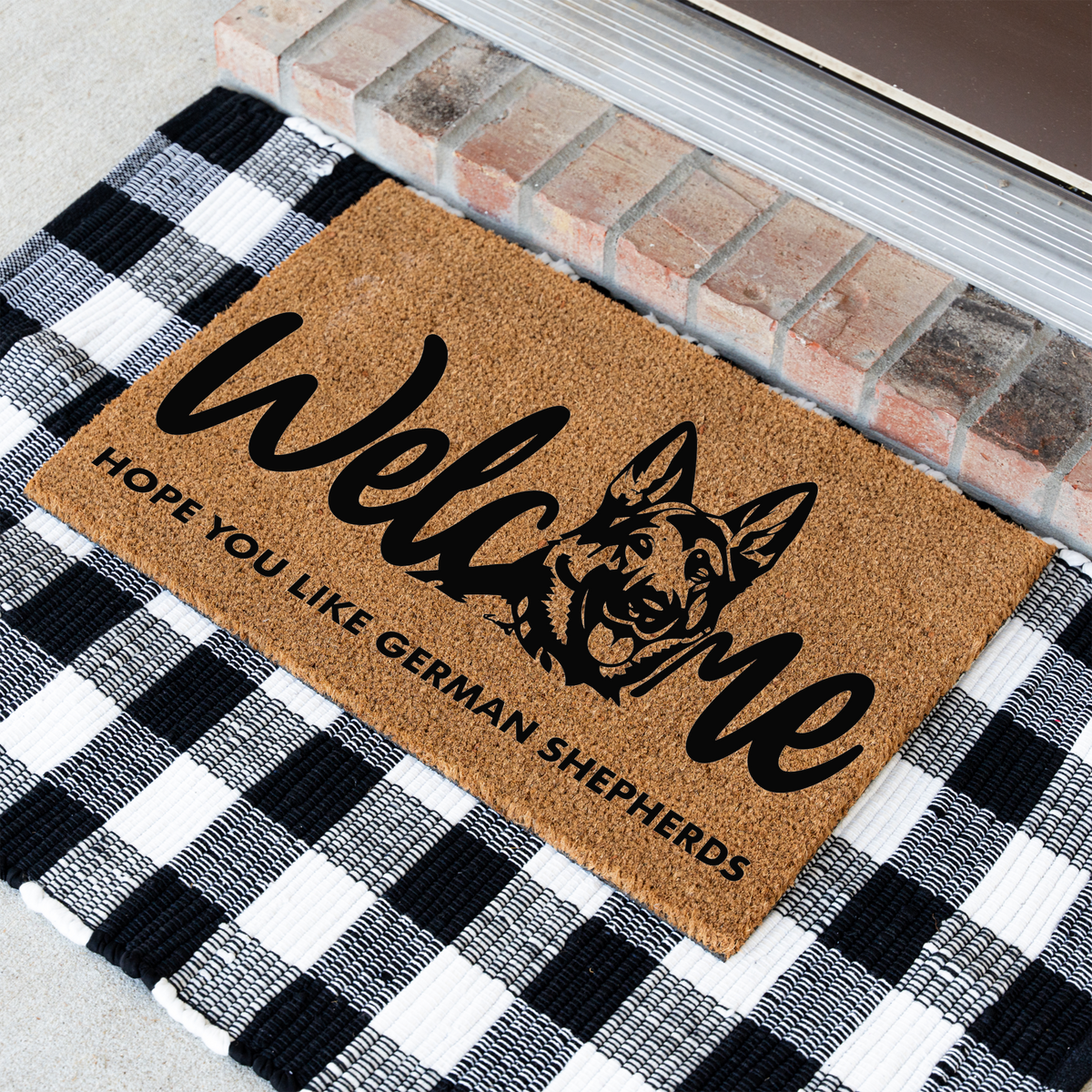 Welcome Hope You Like German Shepherds coir doormat with a German shepherd head in the word welcome at an angle on a black and white buffalo check rug