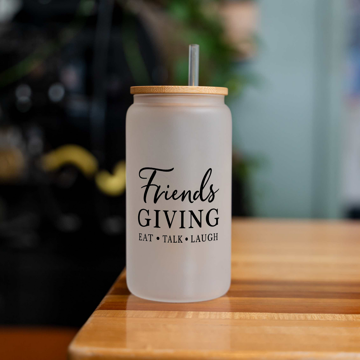 Friendsgiving 16 oz frosted glass can with a bamboo lid and straw, empty, on a wood table