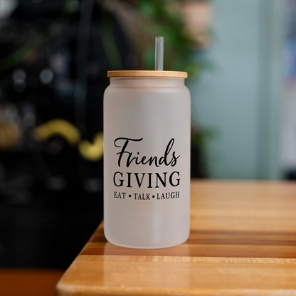 Friendsgiving 16 oz frosted glass can with a bamboo lid and straw, empty, on a wood table