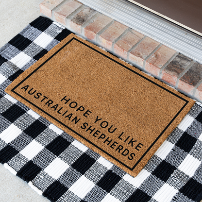 Hope You Like Australian Shepherds minimalist coir doormat with a thin black border at an angle on a black and white buffalo check rug