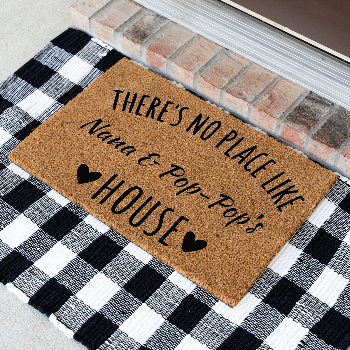 There's No Place Like Nana & Pop-Pop's House coir doormat at an angle on a black and white buffalo check rug