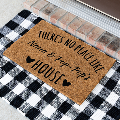 There's No Place Like Nana & Pop-Pop's House coir doormat at an angle on a black and white buffalo check rug