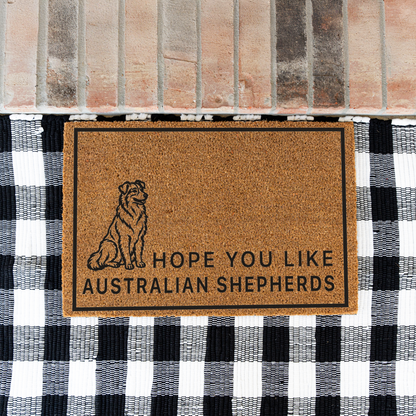 Hope You Like Australian Shepherds coir doormat with a drawing of a sitting Australian shepherd on a black and white buffalo check rug at a brick step