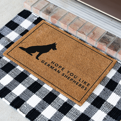 Hope You Like German Shepherds silhouette coir doormat with a thin black border at an angle on a black and white buffalo check rug