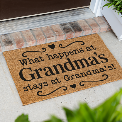 What Happens at Grandma's Stays at Grandma's coir doormat with hearts at an angle on a front porch by a brick step