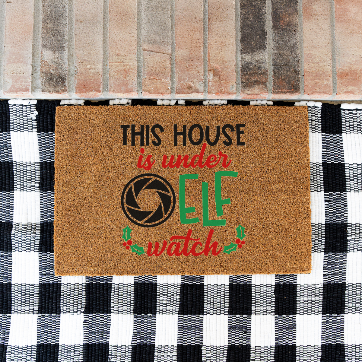 This House Is Under Elf Watch coir doormat on a black and white buffalo check rug at a brick step