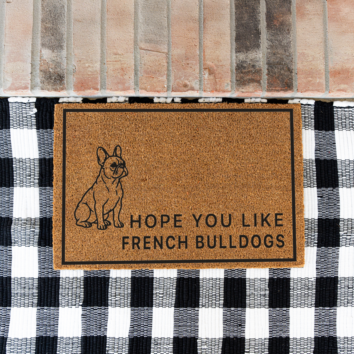 Hope You Like French Bulldogs coir doormat with a drawing of a sitting French bulldog on a black and white buffalo check rug at a brick step