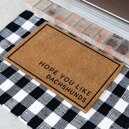 Hope You Like Dachshunds minimalist coir doormat with a thin black border at an angle on a black and white buffalo check rug