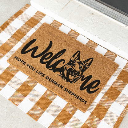 Welcome Hope You Like German Shepherds coir doormat with a German shepherd head in the word welcome on a tan and white check rug