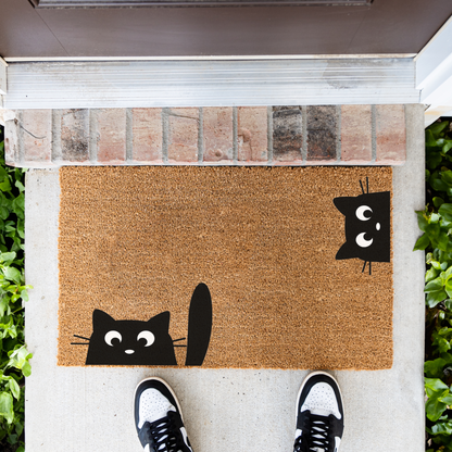 Peeking black cats coir doormat in front of a brick step, top-down view