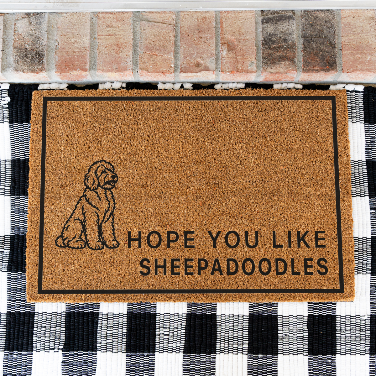 Hope You Like Sheepadoodles coir doormat with a drawing of a sitting Sheepadoodle on a black and white buffalo check rug, close view