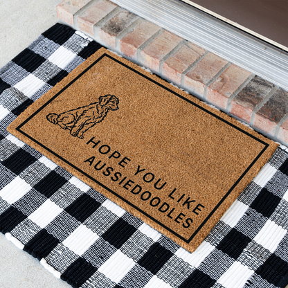 Hope You Like Aussiedoodles coir doormat with a drawing of a sitting Aussiedoodle at an angle on a black and white buffalo check rug