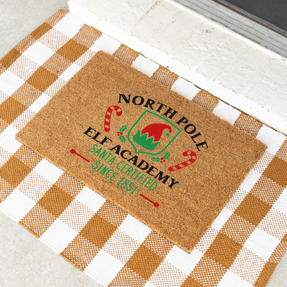 North Pole Elf Academy coir doormat on a tan and white check rug