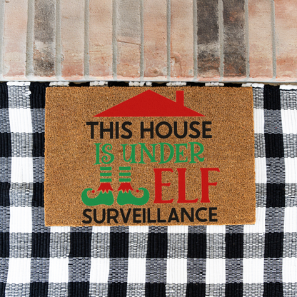 This House Is Under Elf Surveillance coir doormat on a black and white buffalo check rug at a brick step