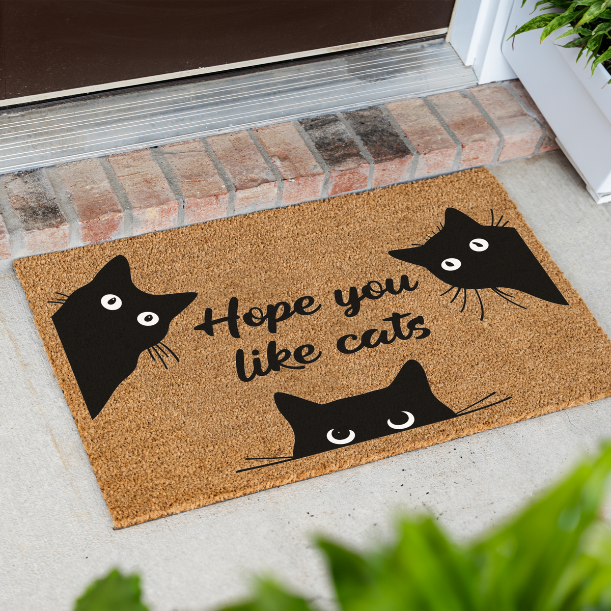 Hope You Like Cats coir doormat with three peeking black cats at an angle on a front porch by a brick step