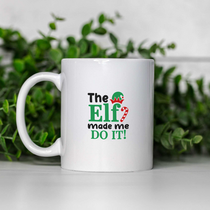 The Elf Made Me Do It white ceramic Christmas coffee mug on a white shelf with greenery