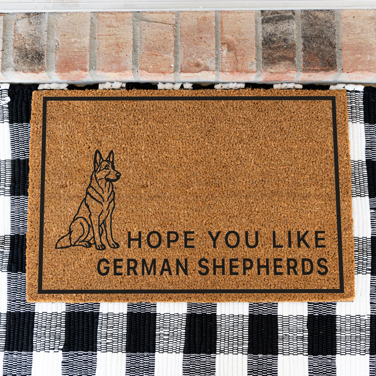 Hope You Like German Shepherds coir doormat with a drawing of a sitting German shepherd on a black and white buffalo check rug, close view
